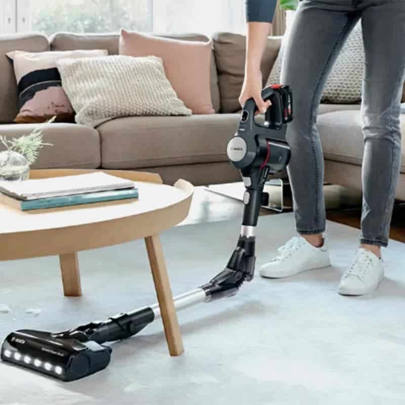 جاروشارژی عصایی بوش مدل Bosch BCS711GB در دست یک مرد درحال جارو زدن زیر میز