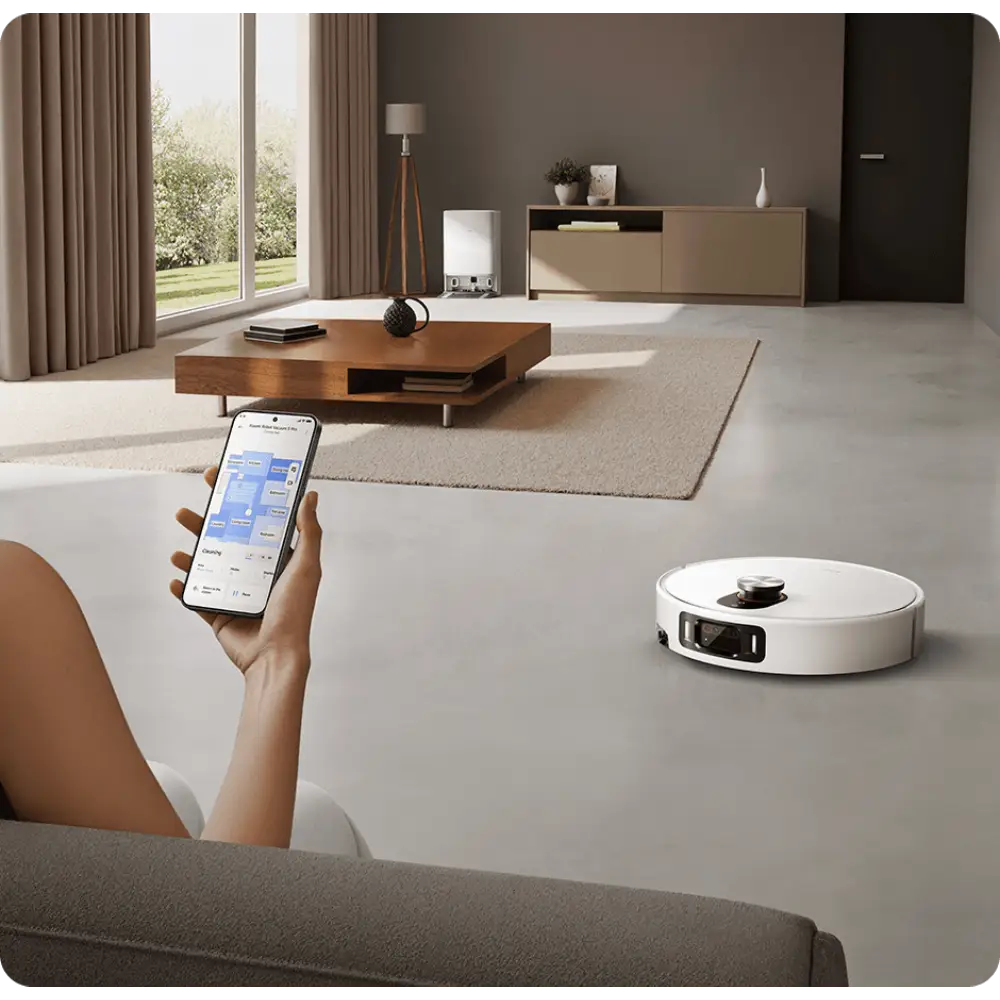 جارو رباتیک شیائومی مدل Robot Vacuum 5 Pro روی زمین و جلوی خانومی که با گوشی و نرم افزار شیائومی در حال کنترل جارورباتیک است